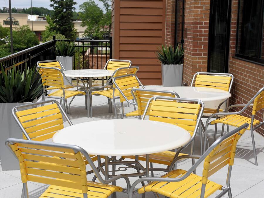 A patio with yellow chairs and white tables, surrounded by brick walls and potted plants.