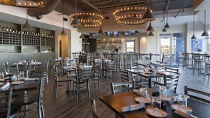 A spacious restaurant with multiple dining tables and chairs, a bar area with shelves of bottles, and a modern industrial ceiling design. - SpringHill Suites by Marriott Orange Beach (Orange Beach)