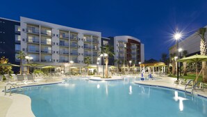 A swimming pool with lounge chairs and umbrellas, surrounded by a hotel building with multiple balconies and palm trees. - SpringHill Suites by Marriott Orange Beach (Orange Beach)