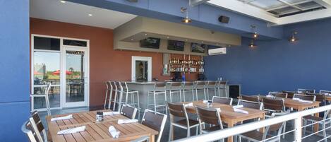 An outdoor dining area with tables and chairs, a bar, and a glass ceiling.