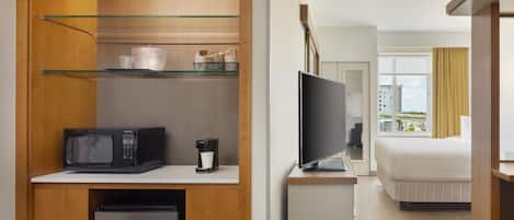 Una habitación de hotel con kitchenette, una cama, un televisor y un ventanal con vistas a edificios.