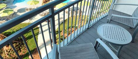 A balcony with a pool view, outdoor seating, and a railing.