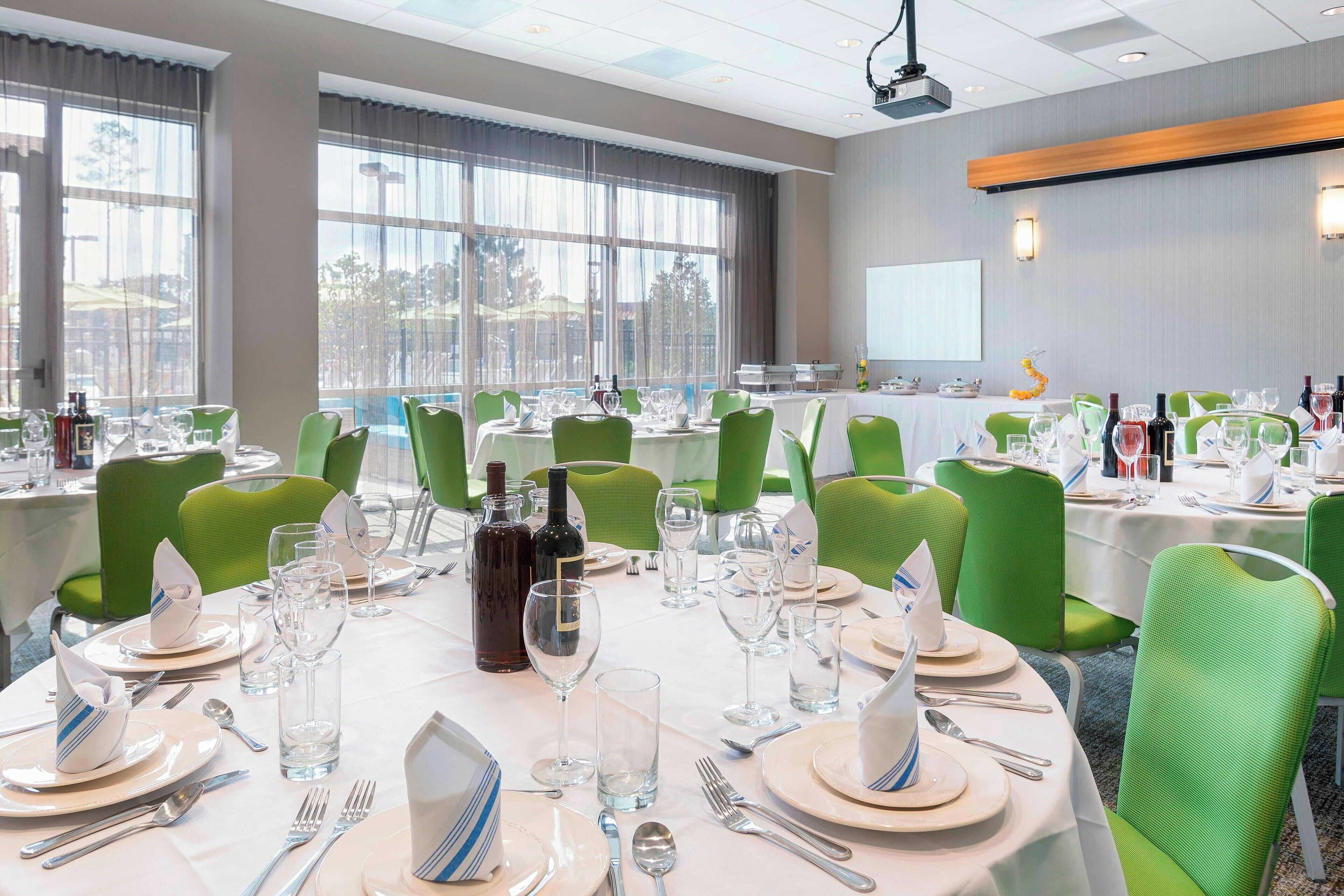 Un salón de conferencias con mesas redondas dispuestas para una reunión, equipado con sillas, platos, cubiertos y botellas de vino.