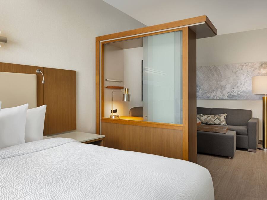 Ein Hotelzimmer mit einem großen Bett, einem Holzkopfende, einem Nachttisch, einem Spiegel, einer Couch und einer Lampe.