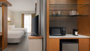 A hotel room with a bed, a TV, a microwave, a coffee maker, and a small refrigerator.