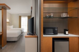 A hotel room with a bed, a TV, a microwave, a coffee maker, and a small refrigerator.