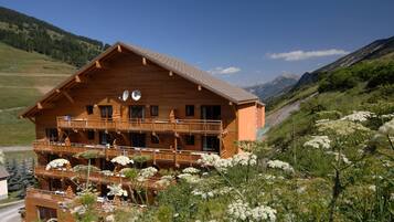 Un chalet en bois doté de nombreux balcons, entouré d’un paysage montagneux et d’une végétation luxuriante.