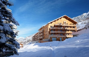 A multi-story wooden building with balconies, surrounded by snow-covered mountains. - Résidence Odalys Pra Sainte Marie (Vars)