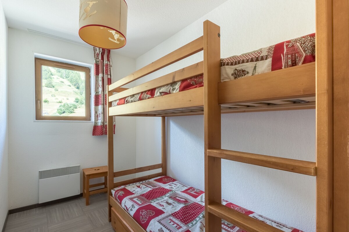 Une chambre avec un lit superposé, une fenêtre, un radiateur et une petite table.