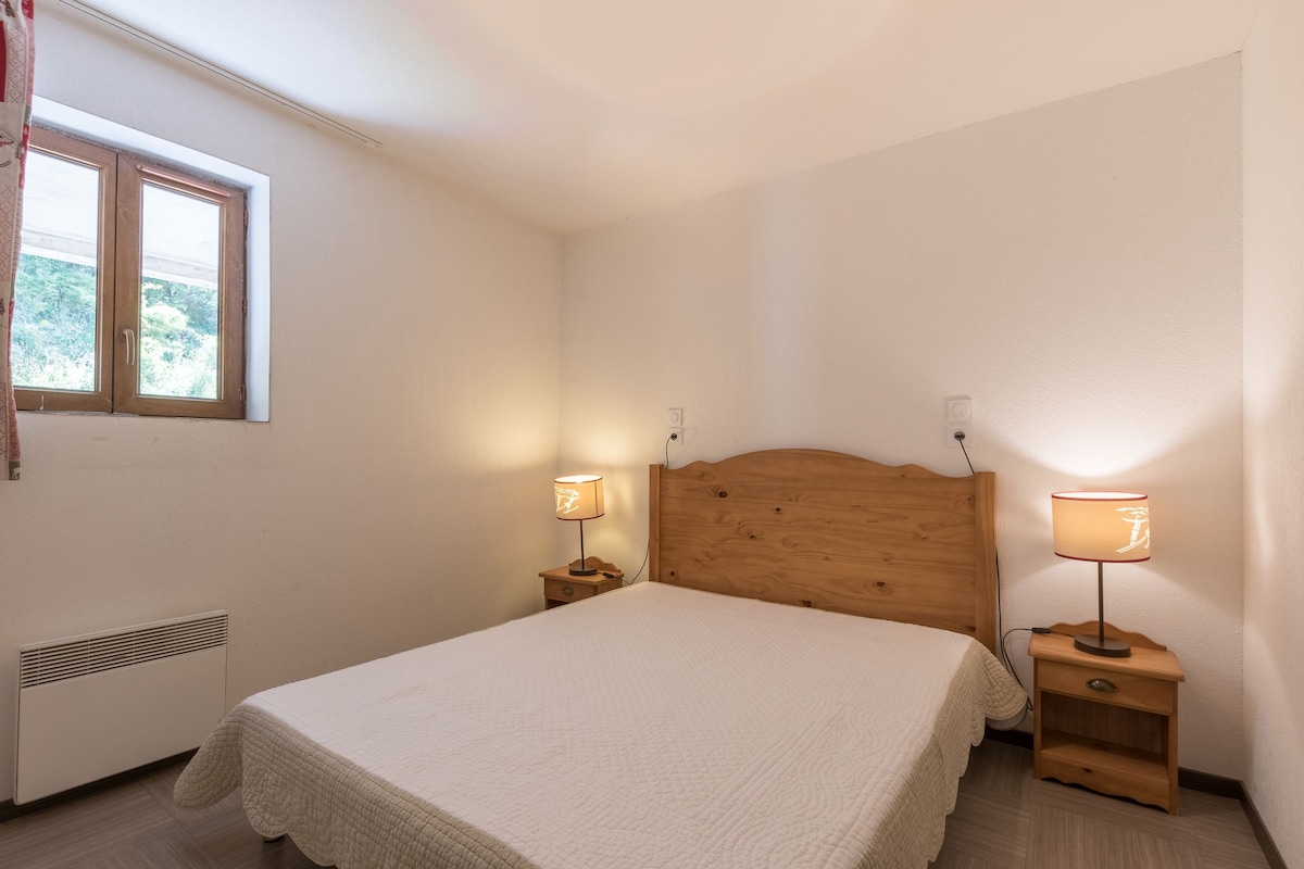 A bedroom with a single bed, two bedside tables with lamps, a window with curtains, and a radiator.