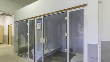 Een rij privé toiletcabines met glazen tussenschotten, een bordje met daarop Hamam en een betegelde vloer.