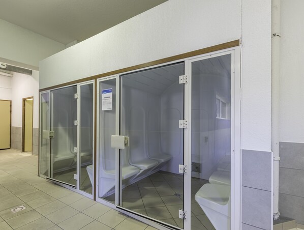 A row of private toilet cubicles with glass partitions, a sign indicating a Hamam, and a tiled floor.