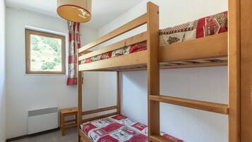 Une chambre avec un lit superposé, une fenêtre, un radiateur et une petite table.
