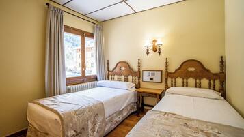 Habitación de hotel con dos camas individuales, cabecera de madera, mesita de noche, ventana con cortinas y lámpara fijada a la pared.