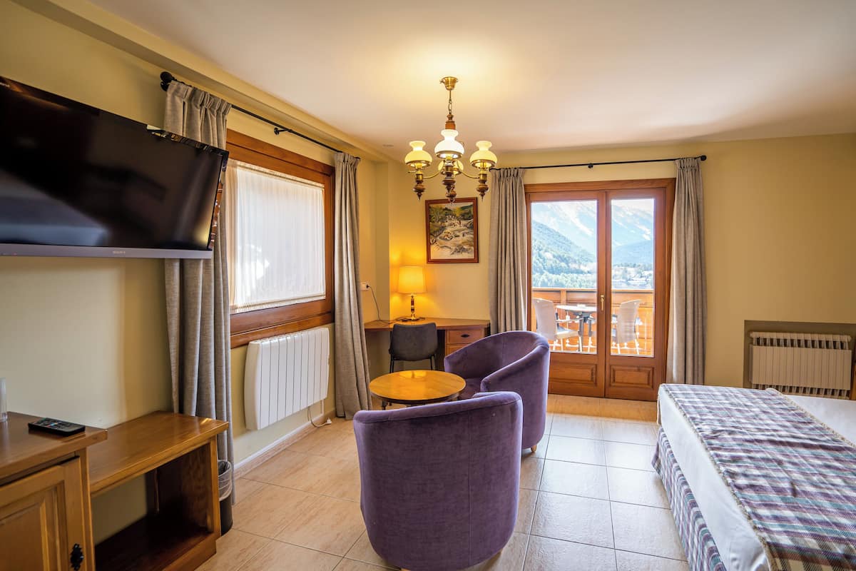 Une chambre d’hôtel équipée d’un lit, d’un bureau, d’une chaise, d’une télévision, d’une lampe et offrant une vue sur les montagnes par la fenêtre.