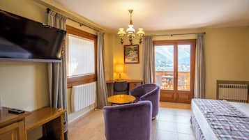 Habitación de hotel con cama, escritorio, silla, televisor, lámpara y vista a las montañas por la ventana.