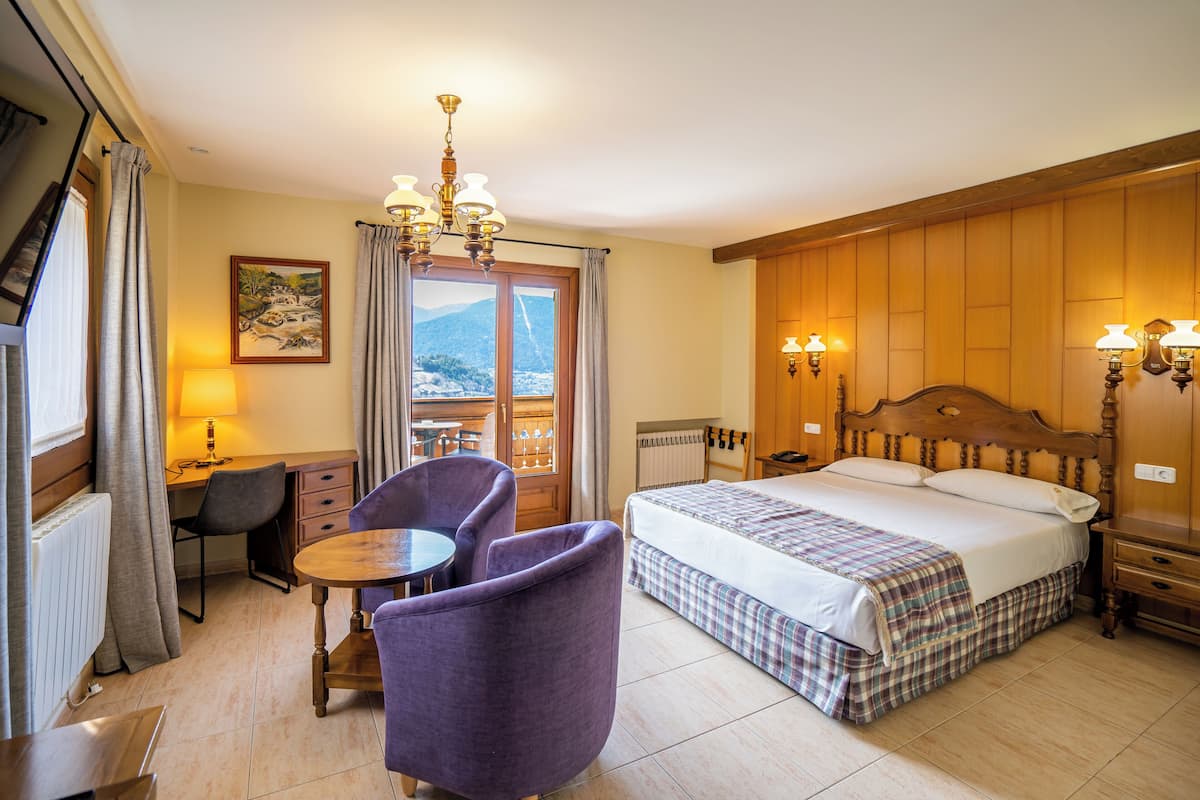 Une chambre d’hôtel avec un lit, un bureau, une chaise, une table et une vue sur les montagnes par la fenêtre.