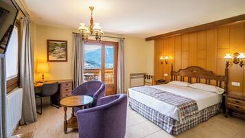 A hotel room with a bed, a desk, a chair, a table, and a view of mountains through the window.