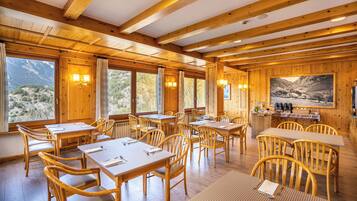 A wooden interior with tables and chairs, large windows, and a mountain view.