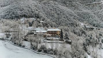 Un paisaje montañoso cubierto de nieve, con un gran edificio de varios pisos y tejado nevado.