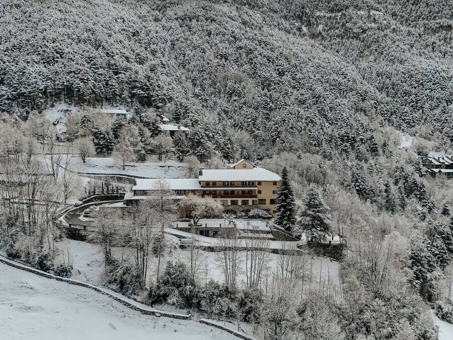 Un paisaje montañoso cubierto de nieve, con un gran edificio de varios pisos y tejado nevado.