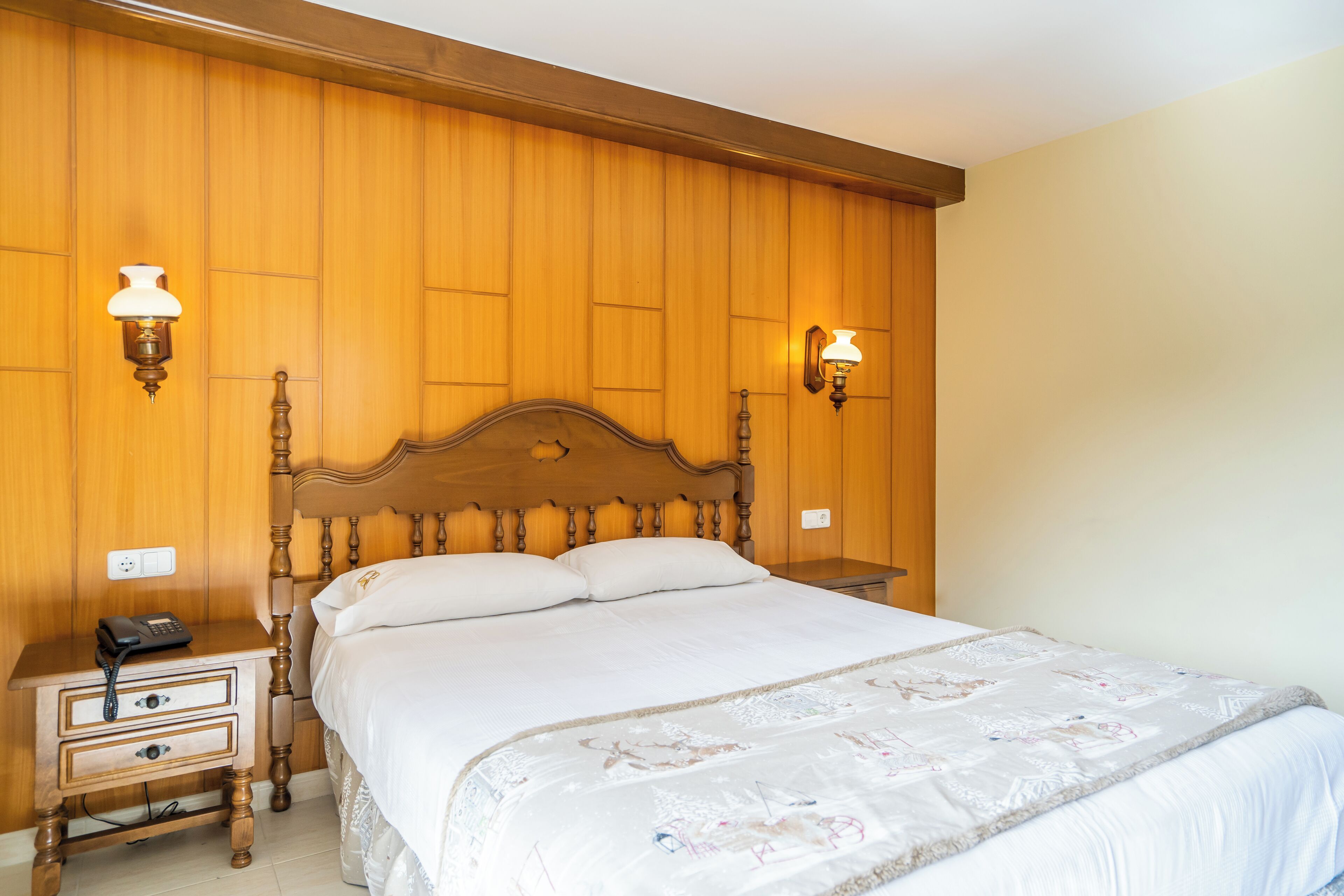 A bedroom with a wooden headboard, a bedside table with a phone, and two wall-mounted lamps.