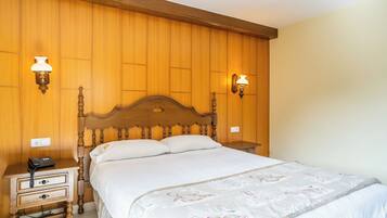 A bedroom with a wooden headboard, a bedside table with a phone, and two wall-mounted lamps.
