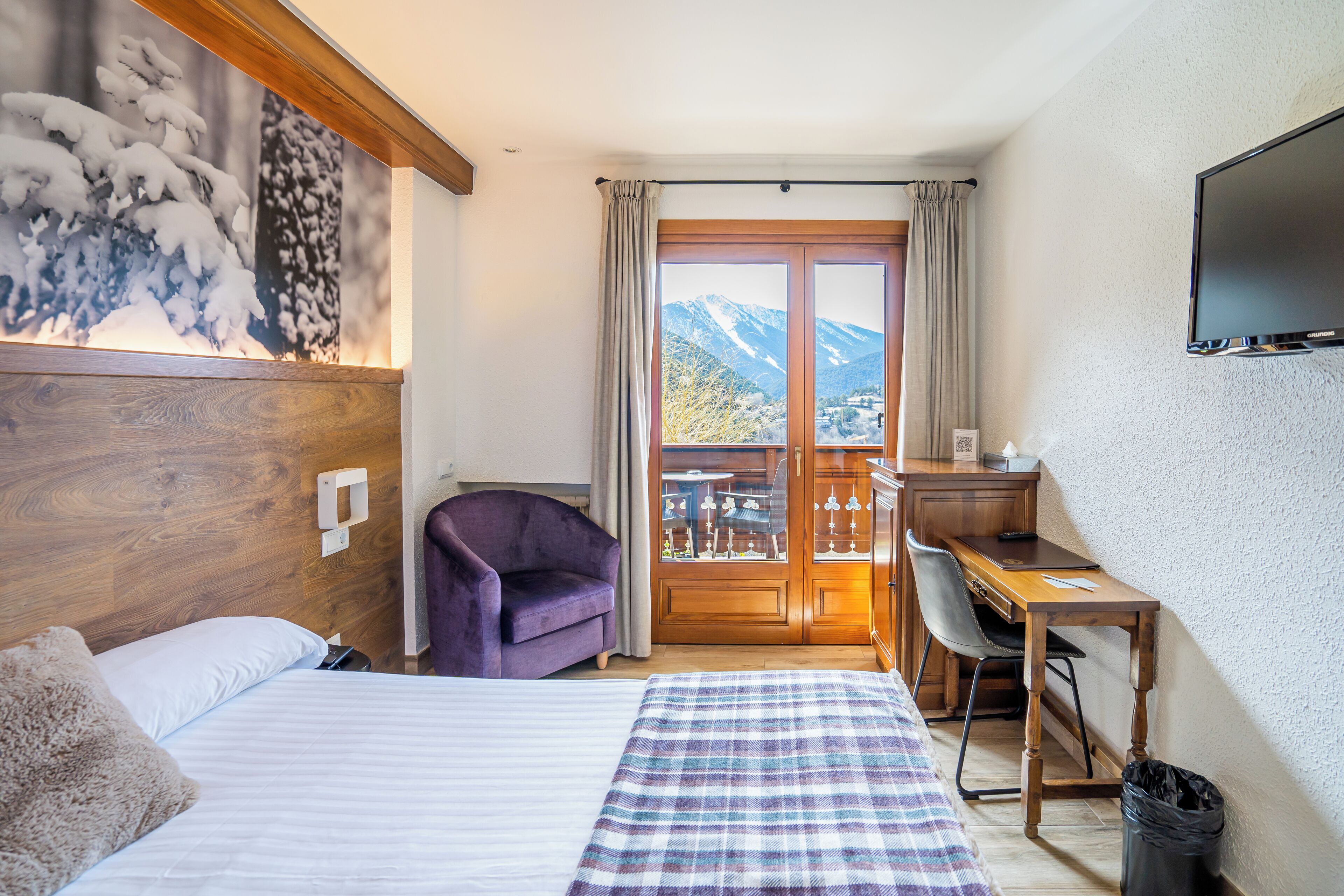 Une chambre d’hôtel équipée d’un lit, d’un bureau, d’une chaise, d’une télévision et d’un balcon avec vue sur la montagne.