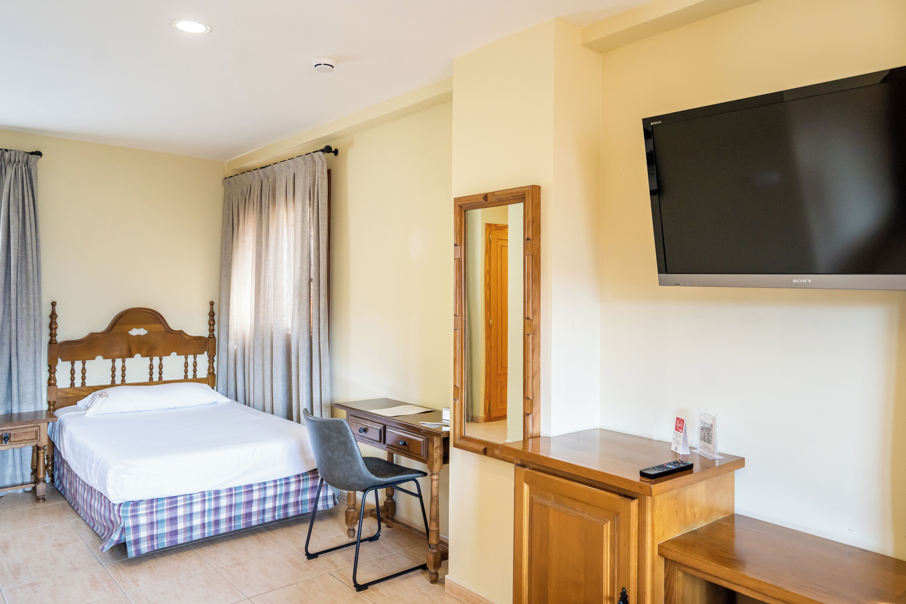 A hotel room with a bed, a desk, a chair, a TV, and a mirror.