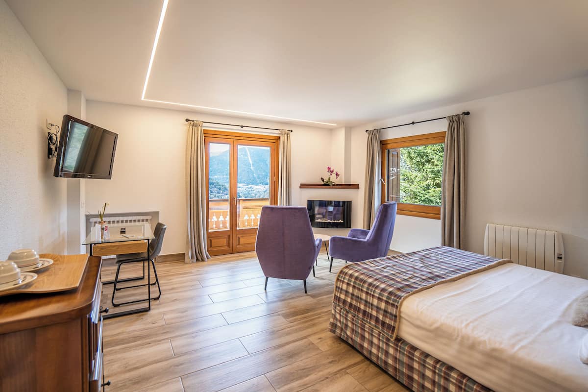 Une chambre d’hôtel comprenant un lit, un bureau avec une chaise, une télévision et une fenêtre avec des rideaux.