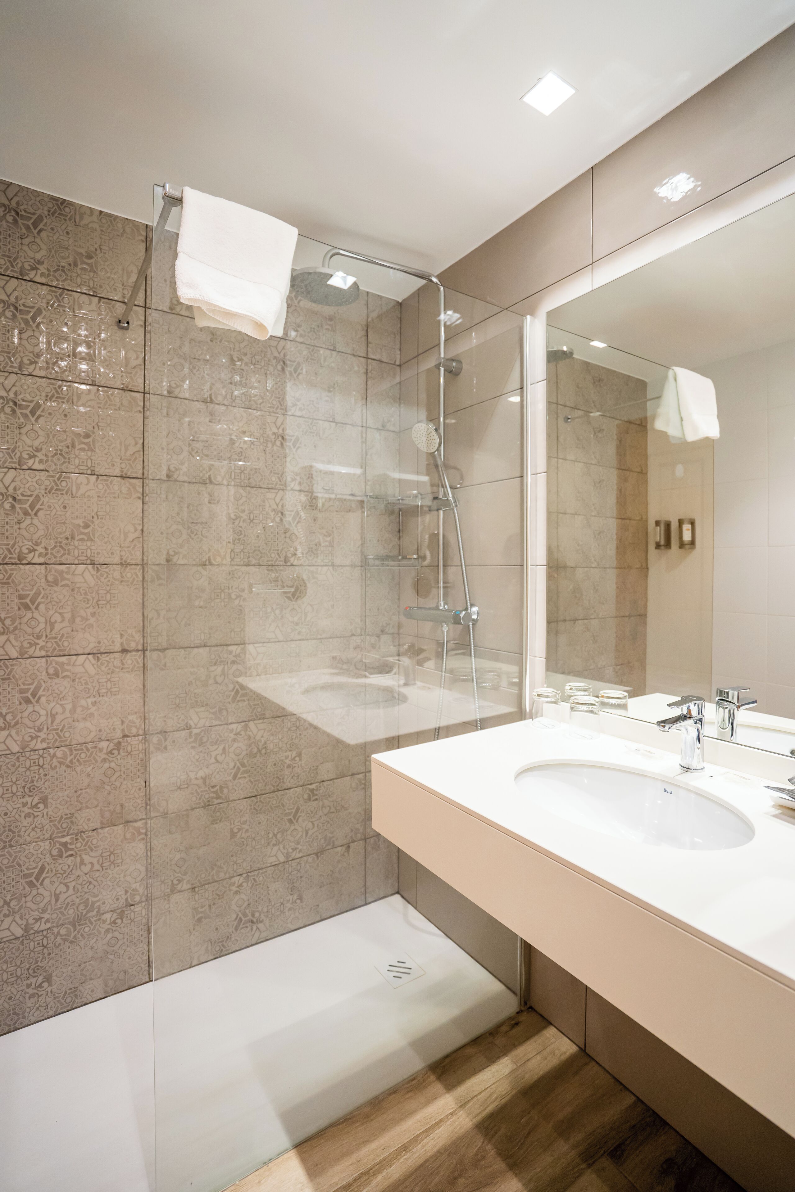 A modern bathroom with a glass-enclosed shower, a large mirror, and a white sink.