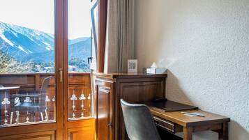 A room with a wooden desk, a chair, a laptop, and a window with a view of mountains.