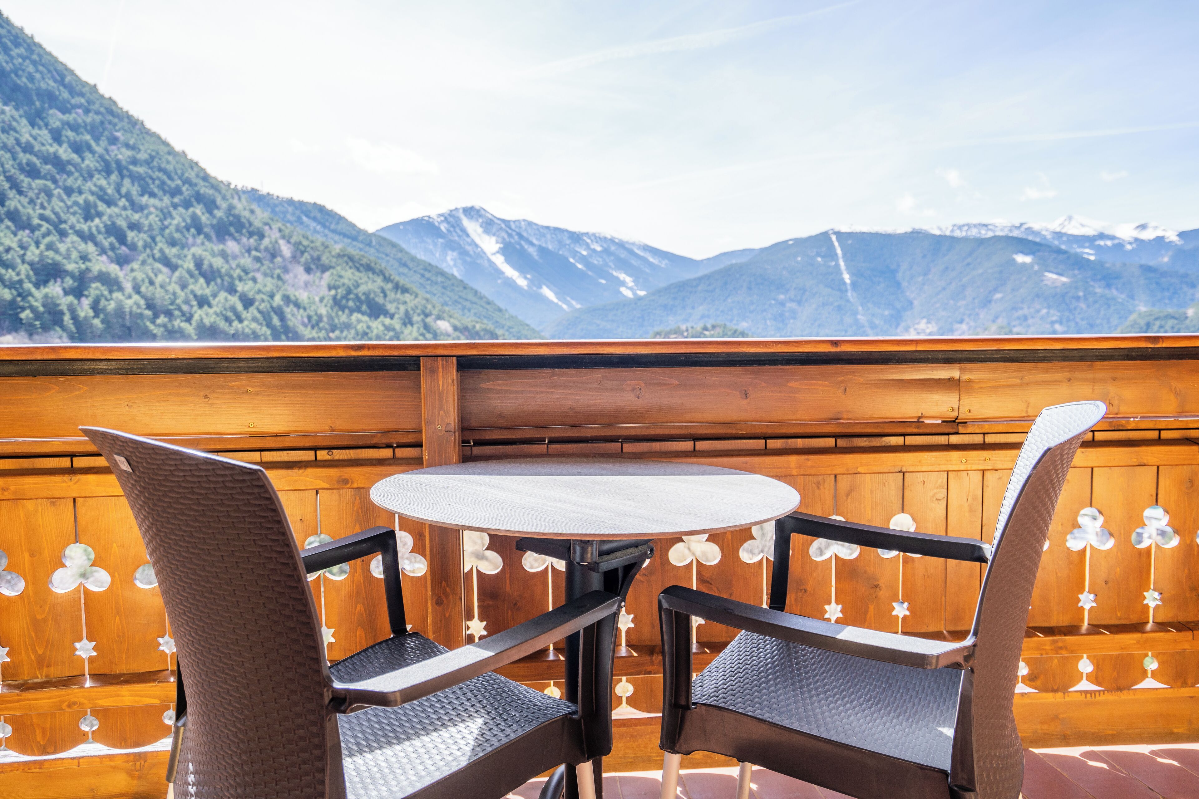 Terraza de madera con una mesa redonda y dos sillas, con vistas a un paisaje montañoso.