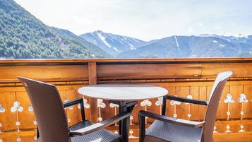 Terraza de madera con una mesa redonda y dos sillas, con vistas a un paisaje montañoso.