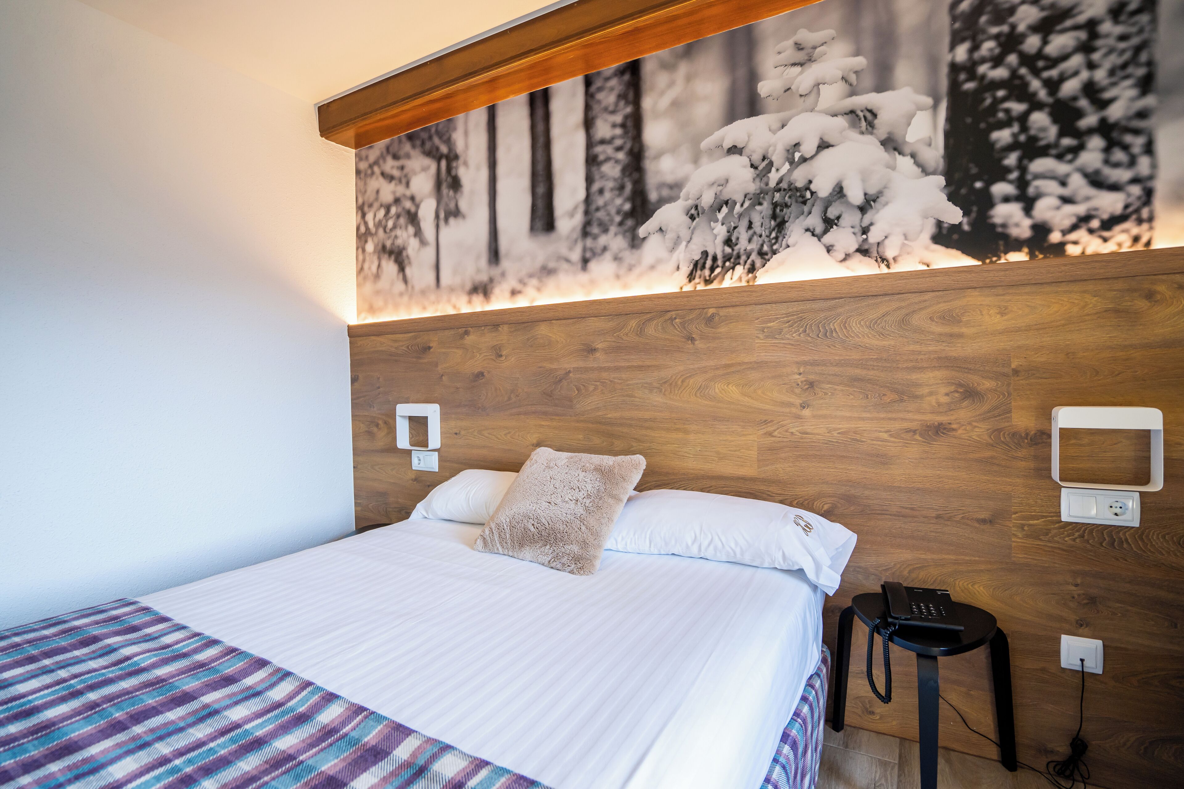 Un lit bien fait, avec une couverture à carreaux, une tête de lit en bois et un téléphone fixé au mur.