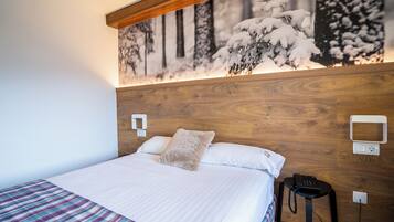 A neatly made bed with a plaid blanket, a wooden headboard, and a wall-mounted phone.