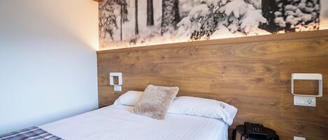 Un lit bien fait, avec une couverture à carreaux, une tête de lit en bois et un téléphone fixé au mur.