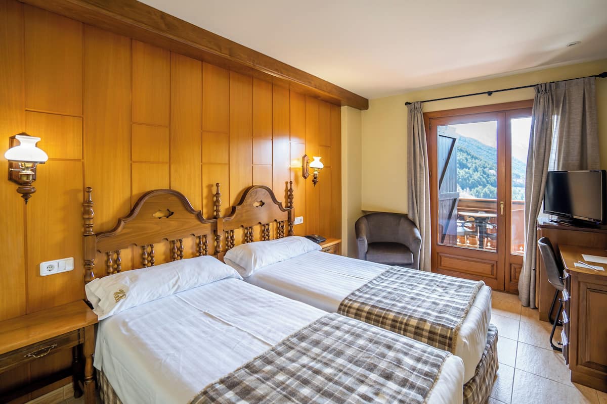 Une chambre d’hôtel avec deux lits, des têtes de lit en bois, un bureau avec une chaise, une télévision et une vue sur l’extérieur.