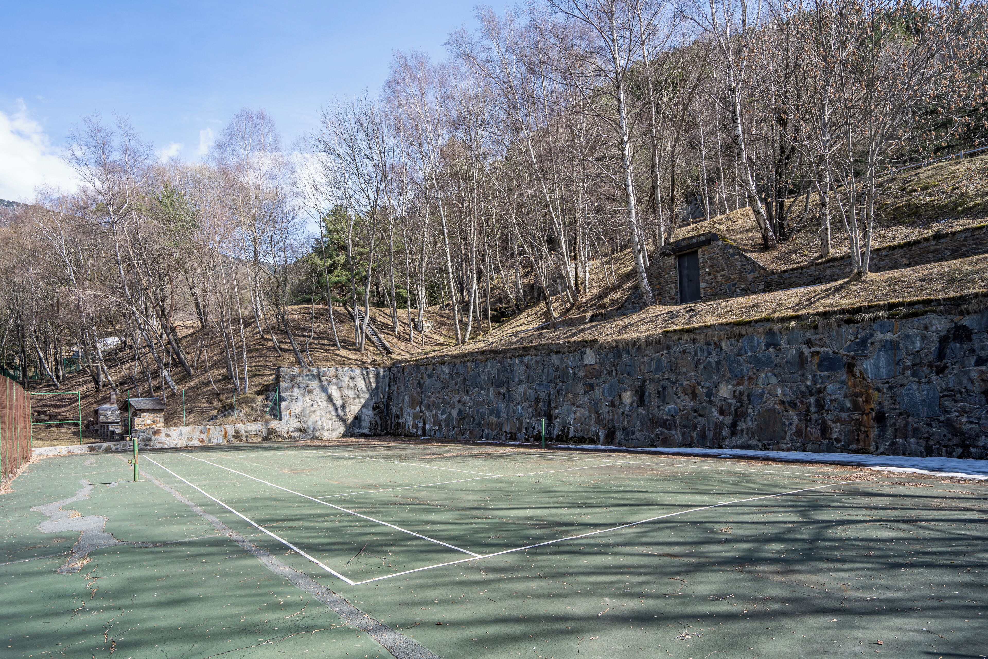 Una cancha de tenis al aire libre con un muro de piedra y árboles al fondo.