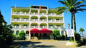 Un hôtel à plusieurs étages, doté de balcons, d’un auvent rouge et de palmiers.