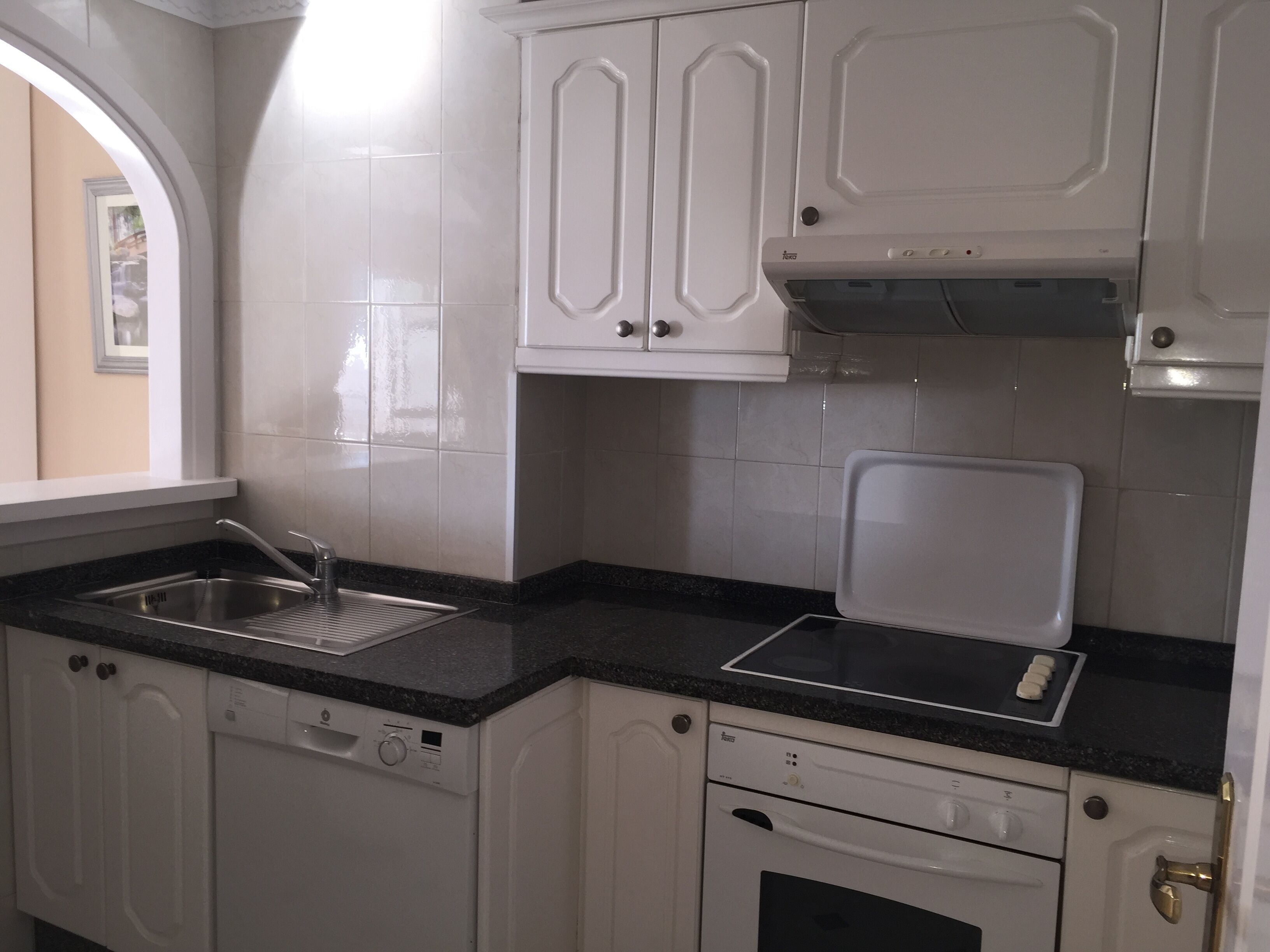 A kitchen with white cabinets, a black countertop, a stainless steel sink, and a dishwasher.