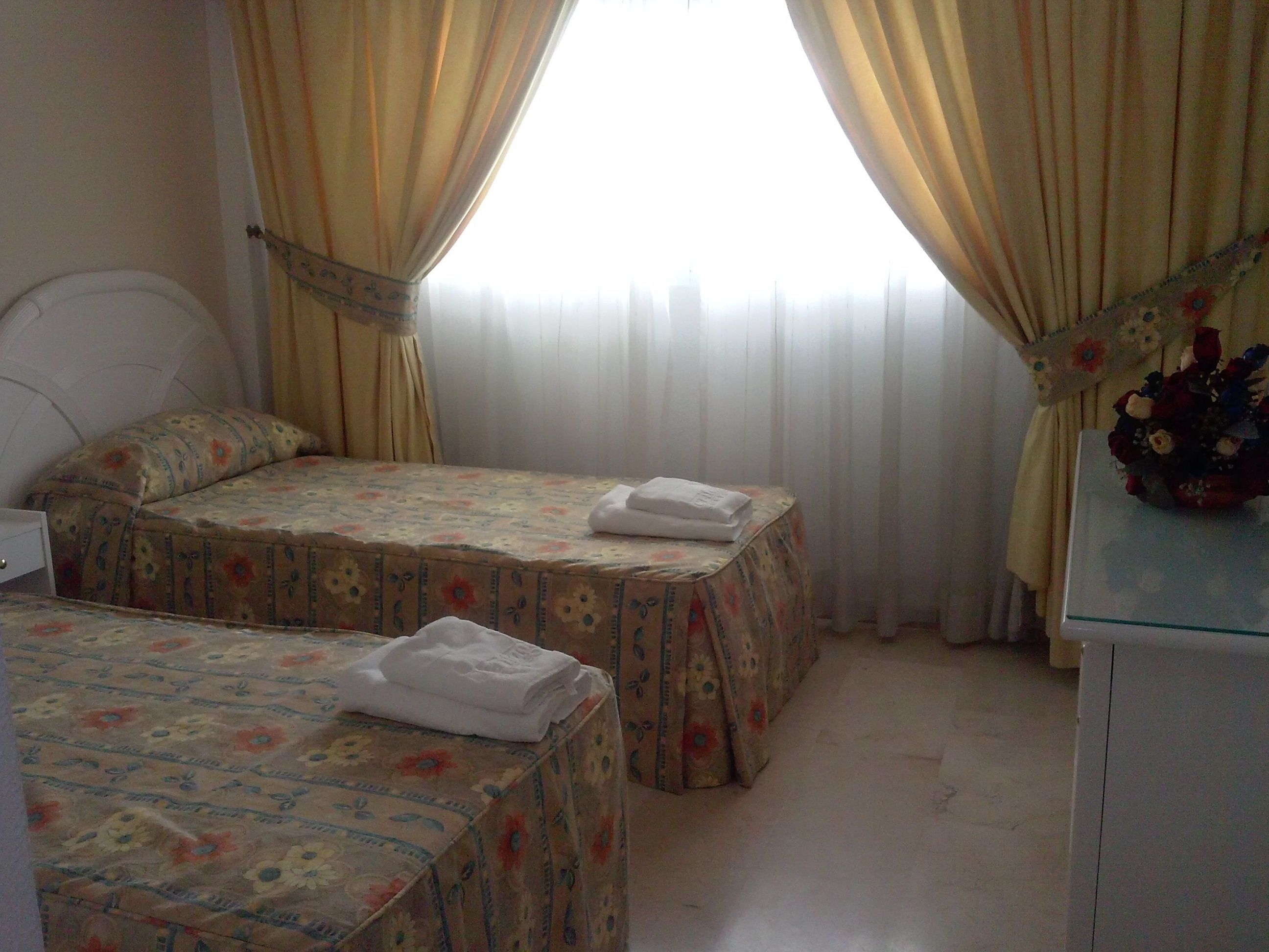 A hotel room with two beds, a small desk, and a window with curtains.