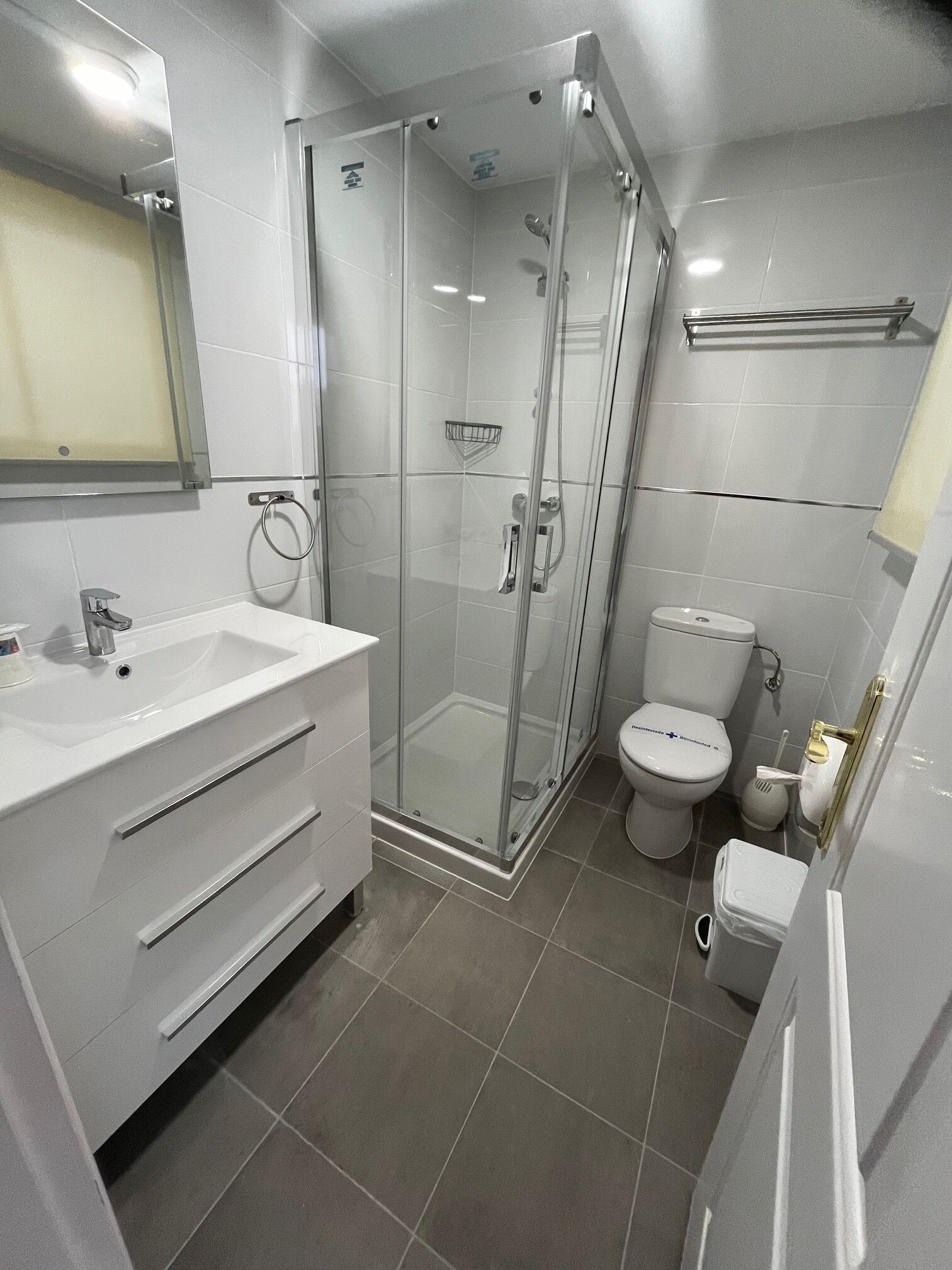 A modern bathroom with a glass-enclosed shower, a white sink with a mirror, and a toilet.