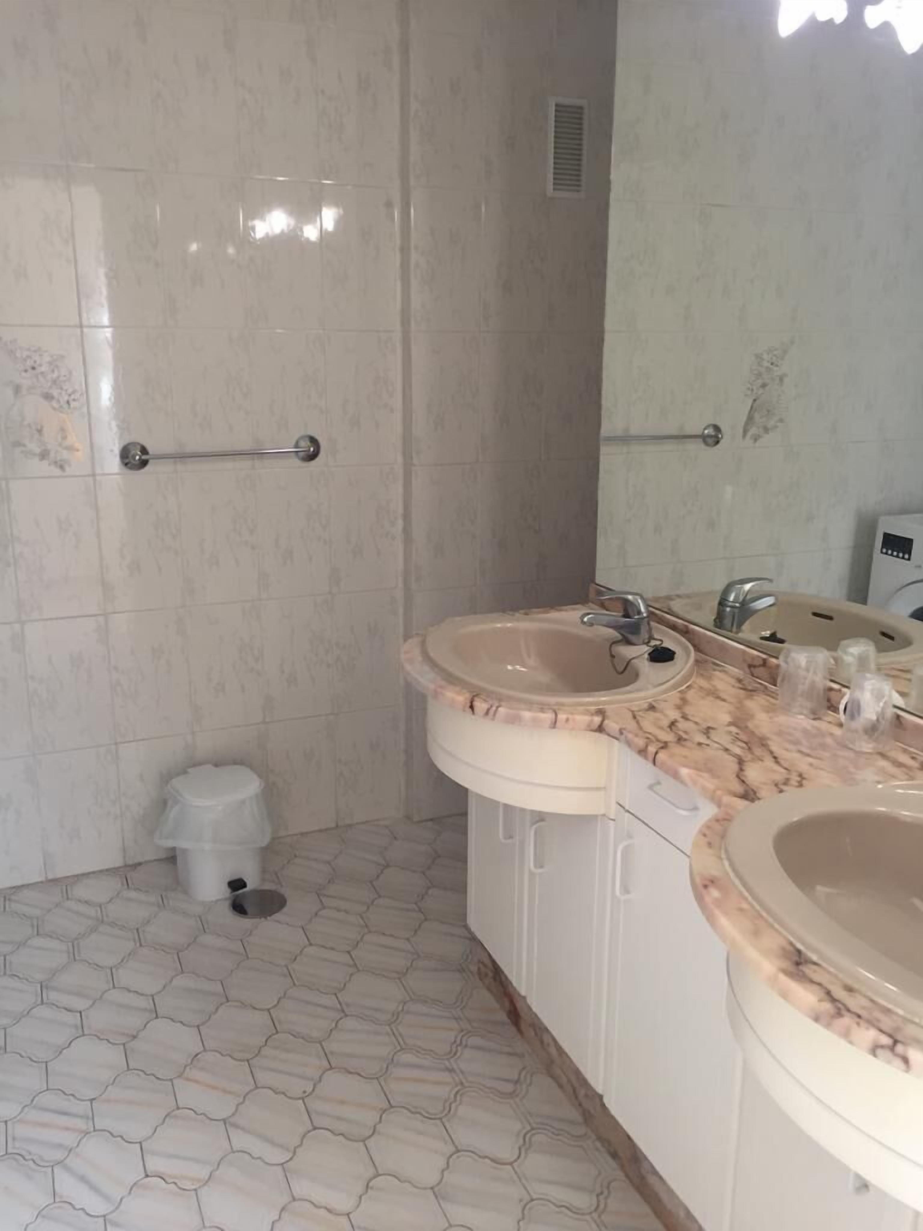 A bathroom with hexagonal patterned floor tiles, two sinks with marble countertops, a hand dryer, and a trash bin.