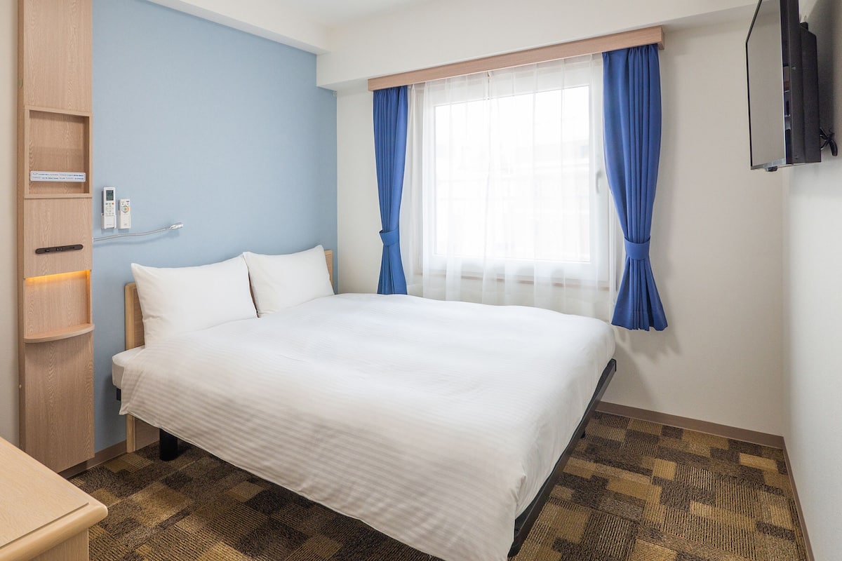 A hotel room with a large bed, a wooden wardrobe, a bedside table, and a TV mounted on the wall.