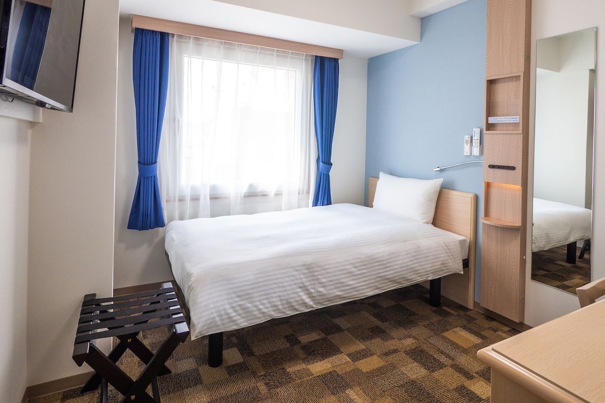 A hotel room with a bed, a small table, a mirror, and a wardrobe.