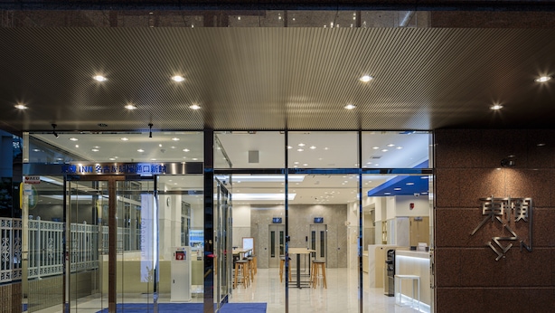 A modern hotel entrance with glass doors, a reception desk, and a seating area visible inside.