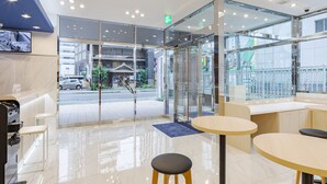 A modern hotel lobby with a glass entrance, seating area, and a view of the street outside.