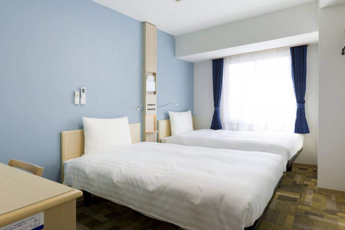 A hotel room with two beds, a desk, and a window with curtains.