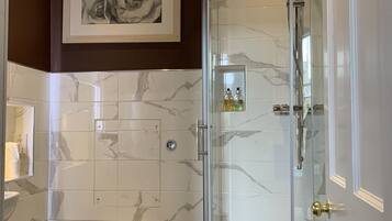 A modern bathroom with a glass-enclosed shower, a toilet, and a marble-tiled wall.